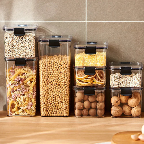 Set of clear storage containers with black lids on a kitchen counter, filled with various dry goods.
